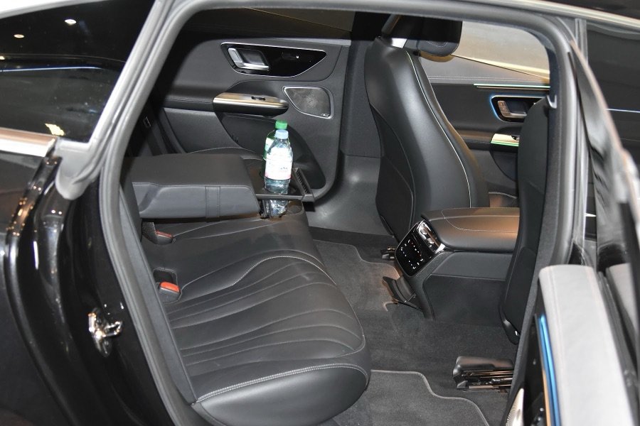 Mercedes EQE rear cabin in black leather, seen through the open door, with bottled water