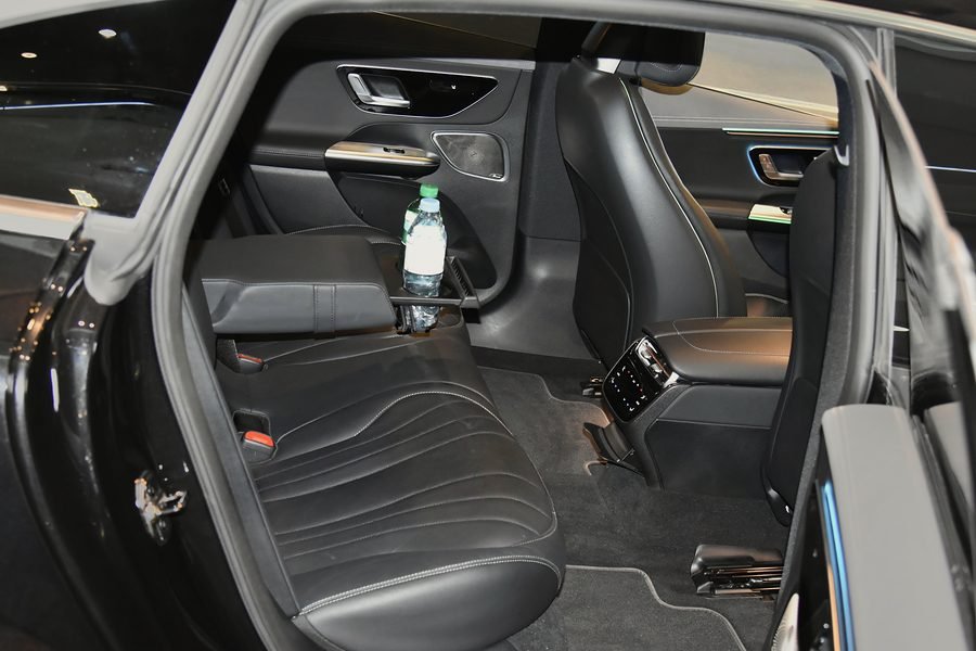 Mercedes EQE rear cabin in black leather, seen through the open door, with bottled water