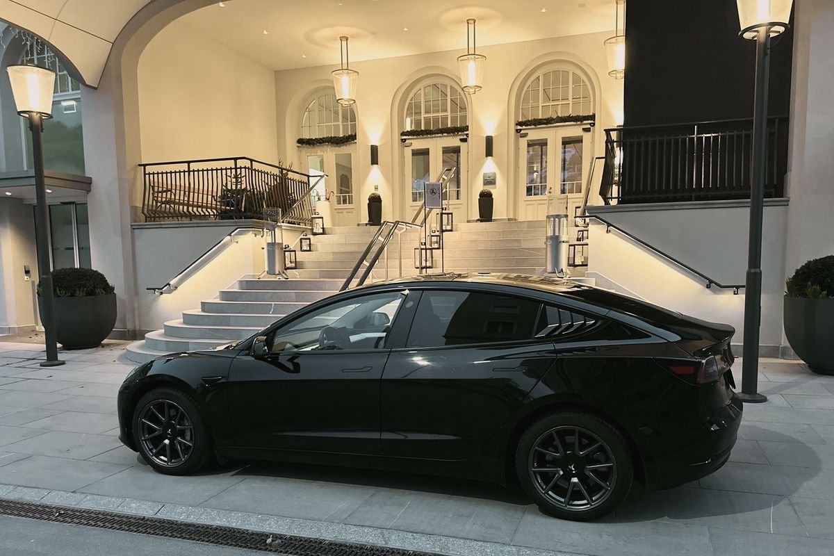 Comfort Sedan: black Tesla Model 3 at a lit hotel entrance