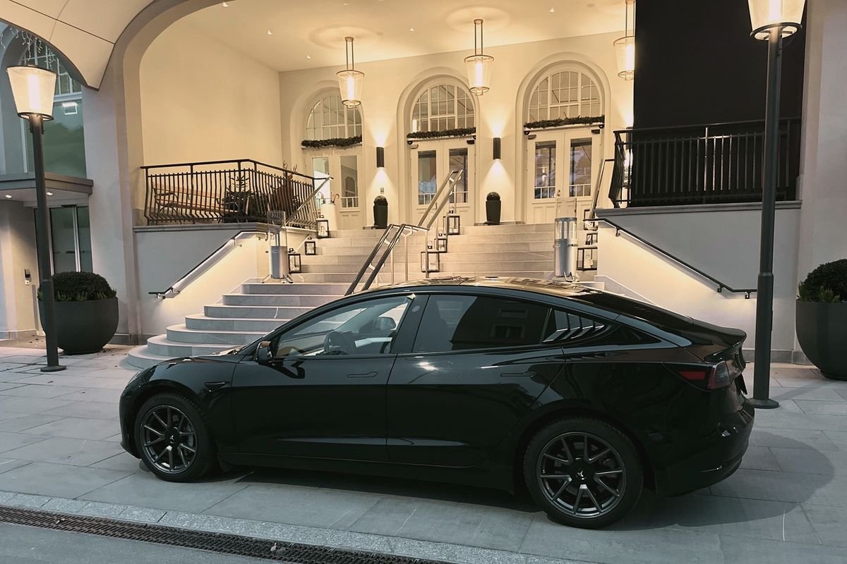 Comfort Sedan: black Tesla Model 3 at a lit hotel entrance