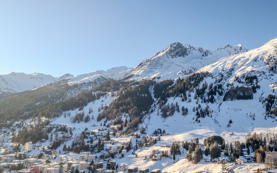 Davos in winter, seen from above: houses at the foot of snow-covered ski slopes under a clear sky