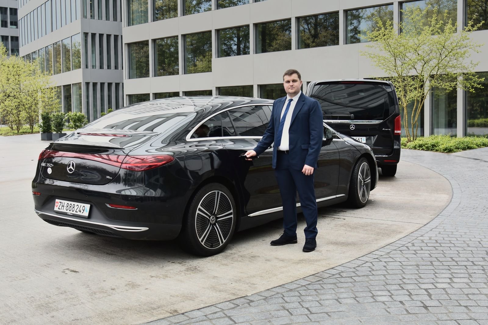 Express Transfer chauffeur in a suit beside a black Mercedes EQE, with a Mercedes V-Class behind