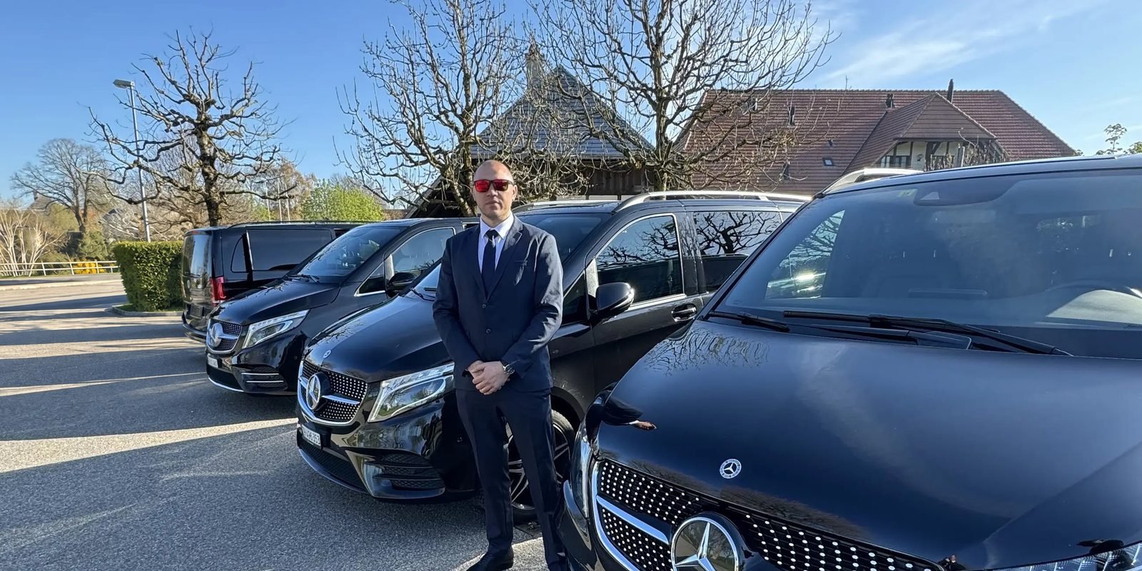 Express Transfer chauffeur in a suit standing beside a row of black Mercedes V-Class vans