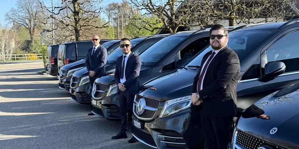 Express Transfer chauffeurs in suits standing beside a row of black Mercedes V-Class vans