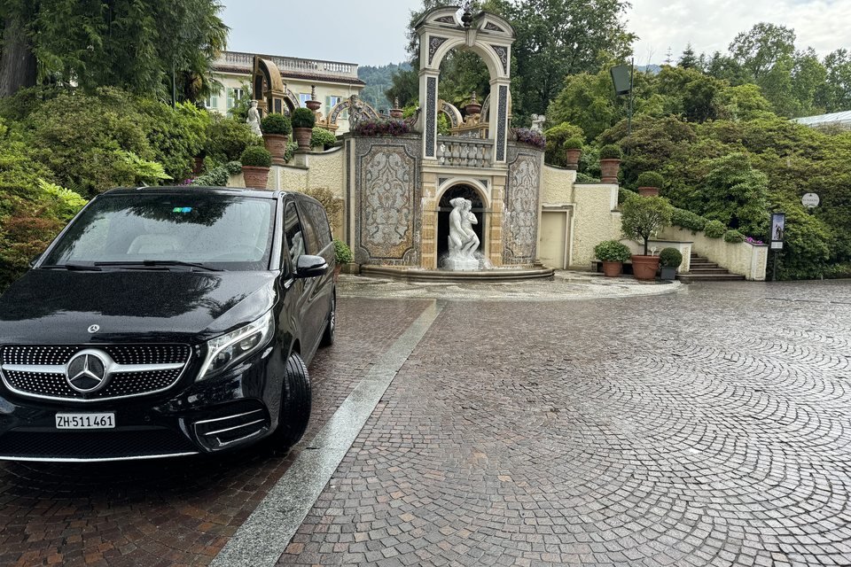 Black Mercedes V-Class from the Express Transfer fleet in the courtyard of a villa, in front of an ornate gate with a fountain statue