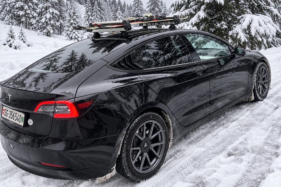 Our black Tesla Model 3 with skis in a roof carrier, parked on a snowy forest road