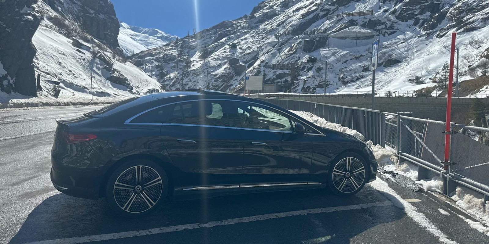 Black Mercedes EQE on a mountain road between snow-covered rock walls under a blue sky