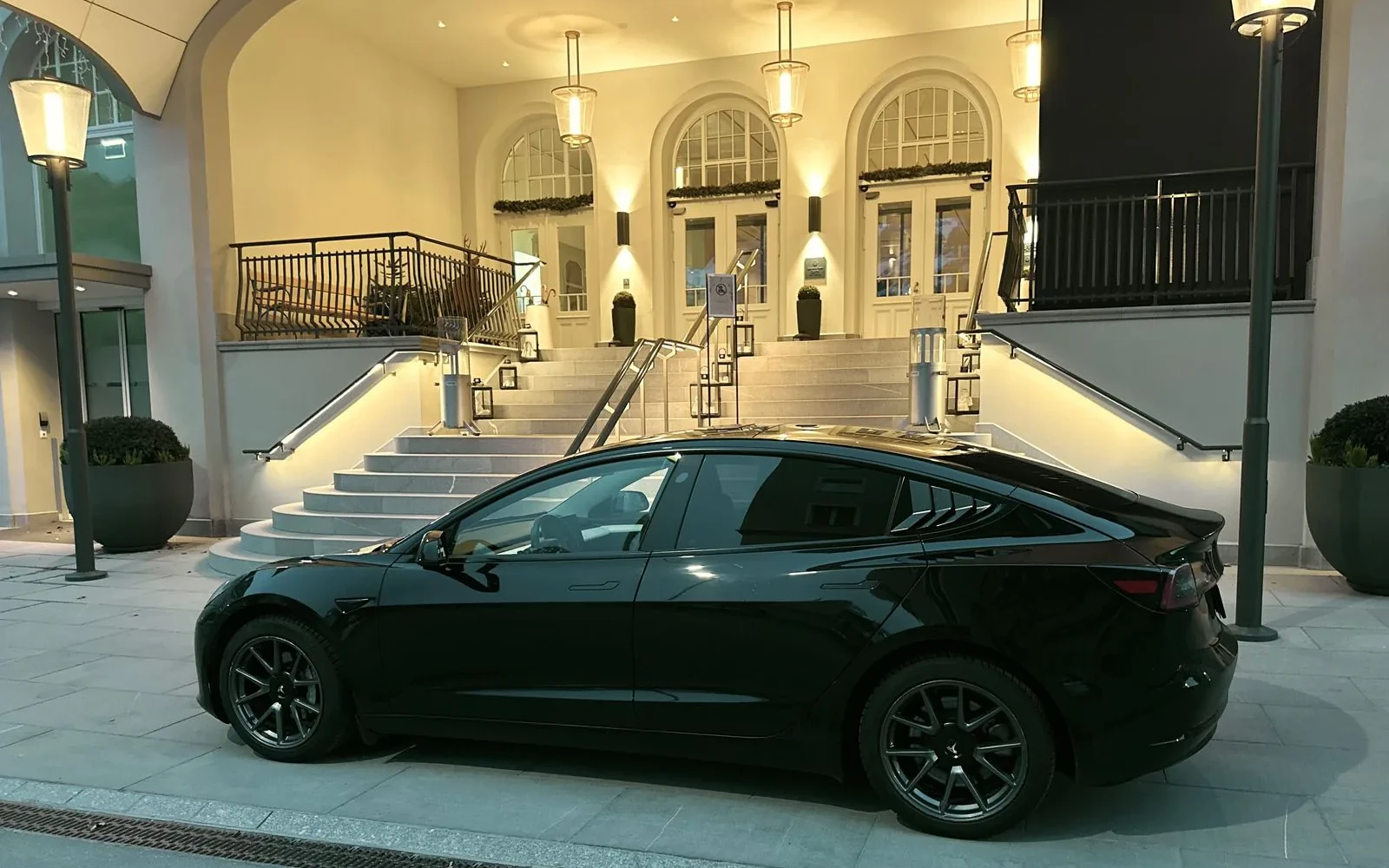 Black Tesla Model 3 parked outside a hotel entrance.