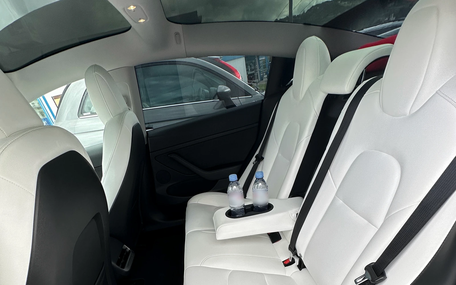 White rear seats, a panoramic glass roof and two water bottles inside a Tesla Model 3.