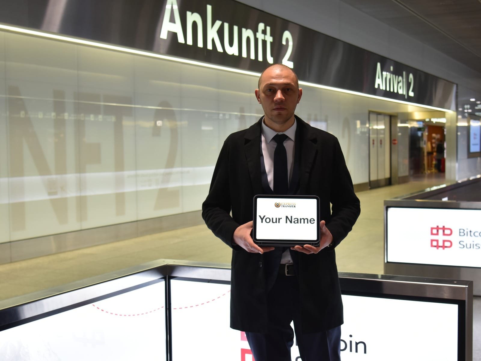 Express Transfer chauffeur holding a name sign beneath the Arrival 2 signs at Zurich Airport.