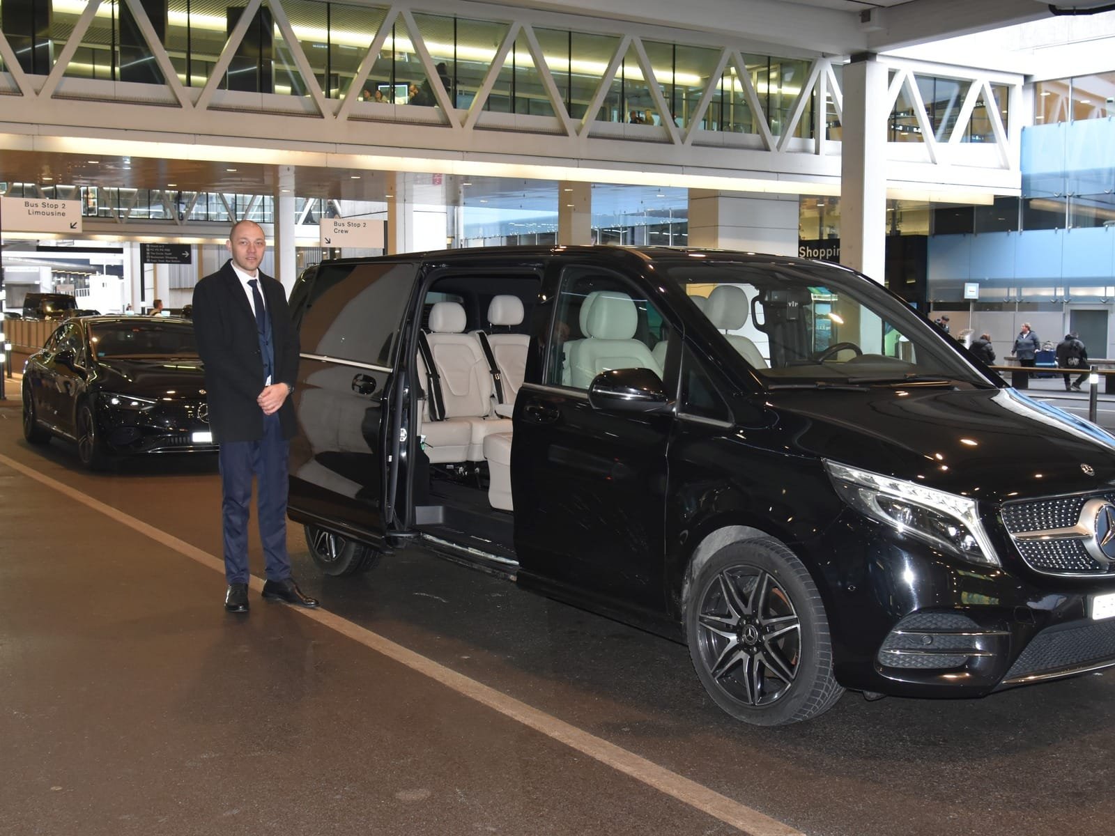 Express Transfer chauffeur standing beside an open Mercedes V-Class at Zurich Airport.