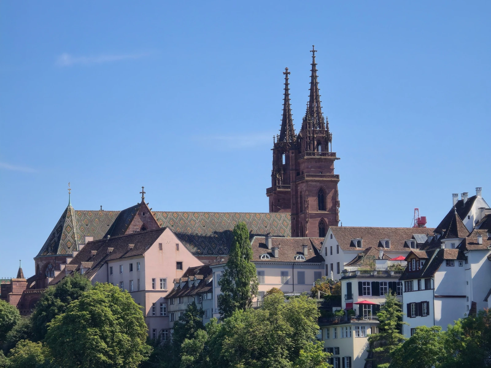 Basel Minster rising above Old Town rooftops under a clear blue sky.
